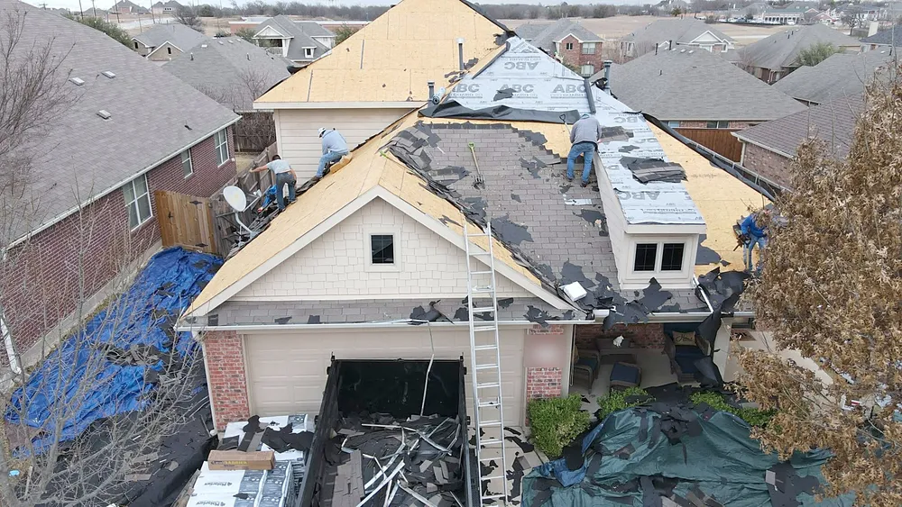 Drone view of a crew stripping a two-story roof, a dump trailer below