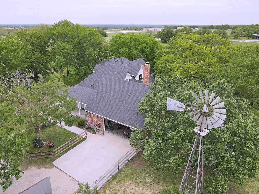 Drone view of a country home with a new dark shingle roof beside a windmill