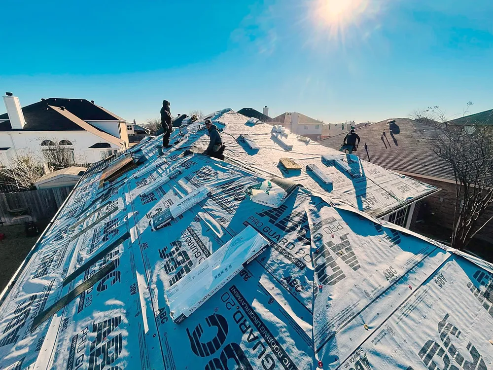 Roofers laying synthetic underlayment across a roof on a sunny day