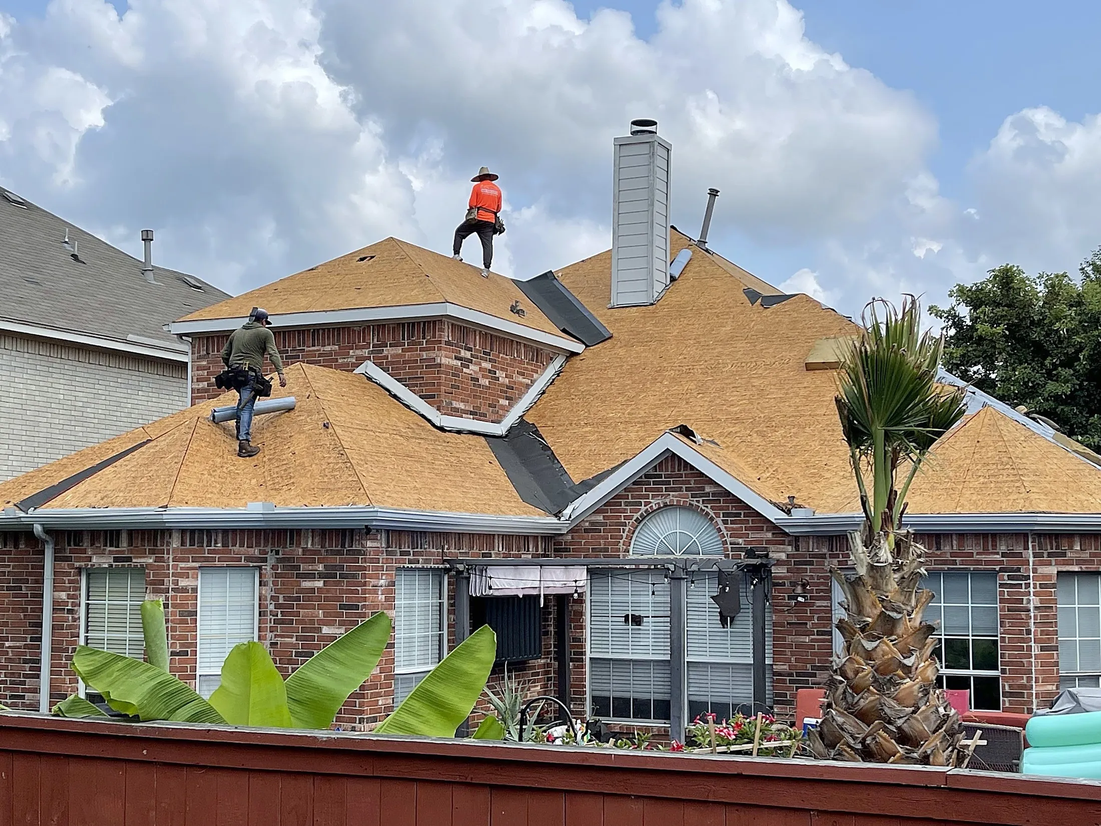 Two NTX Roofing Solutions roofers on a brick home mid-replacement, the whole roof deck covered in orange underlayment